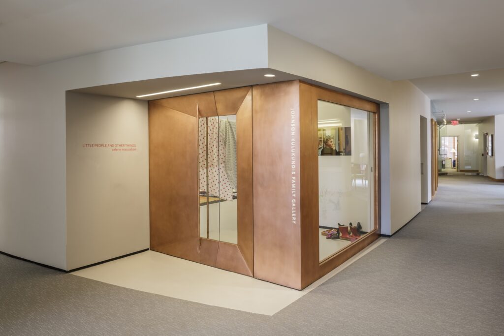 Copper-framed storefront with glass windows in a modern hallway; display shows shoes and a large fashion interior beyond, soft lighting nearby.