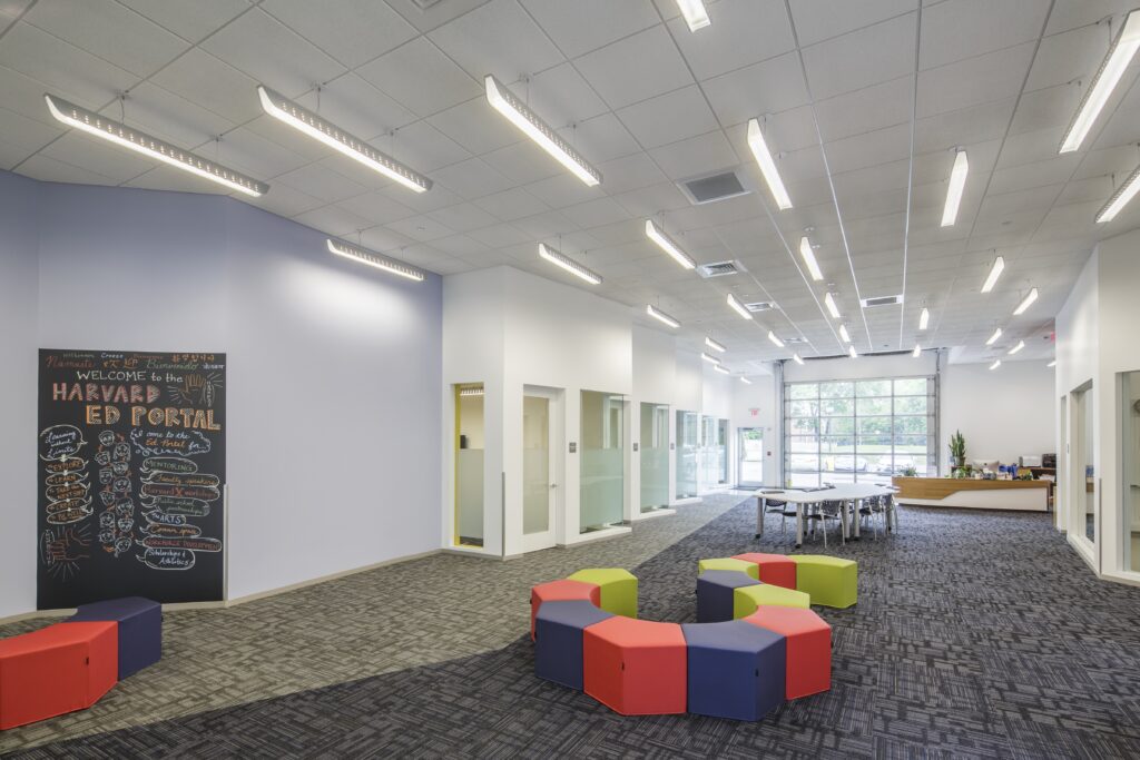 Open communal lounge with colorful cube seats, a chalkboard wall, and large windows at the back of a bright office space.