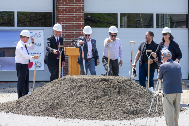 Group of professionals in hard hats at a building's groundbreaking ceremony, shovels in hand around a dirt pile.
